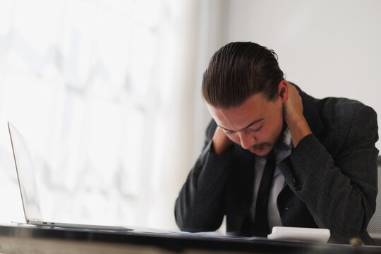 Male professional working on laptop experiencing discomfort and physical pain due to long hours, stress, and fatigue