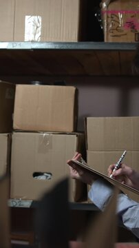 Man carrying a cardboard box through a dim storage room with metal shelves and stacked packages