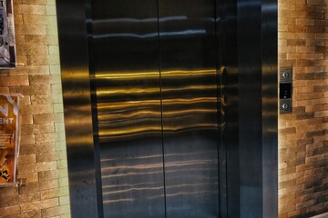 Closed modern elevator doors made of dark stainless steel in a contemporary building lobby with decorative brick stone walls © Satriyo