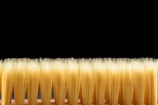 Detailed close-up of a yellow bristle brush with finely aligned hair strands against a black background, macro photography showcasing texture and craftsmanship