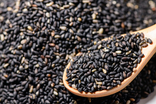 Black roasted sesame seeds close-up on a wooden spoon with scattered seeds, food ingredient and culinary staple for Asian cooking and recipes