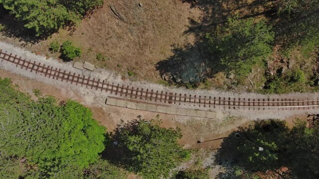 Aerial top view of winding narrow gauge railway curving through green forest in Mokra Gora, Serbia. Small station in mountain, 4k