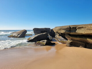 Waves wash around angular boulders and layered rock ledges beside golden sand at Soldiers Point at low tide, Central Coast, New South Wales, Australia. © Diane