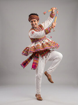 Male Indian folk dancer balancing on one leg with decorated dandiya sticks and embroidered attire