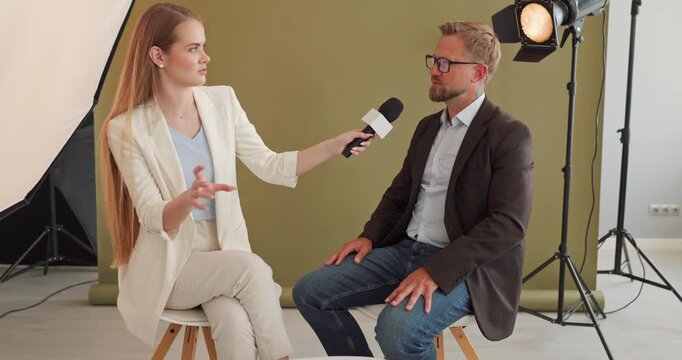 Interview journalist asks guest with microphone in studio. Soft lights and framing support discussion as media crew run camera recording for business production. Clear concept for media work.