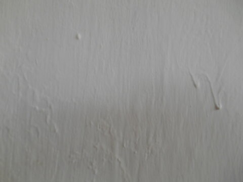 Close up view of a white painted wall texture with bumpy concrete flaws, paint drips, and uneven brush marks. Detailed rough plaster cement surface background for industrial interior design.
