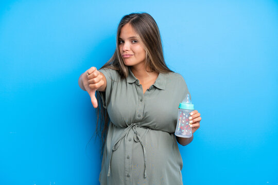 Pregnant woman on blue background showing thumb down with negative expression