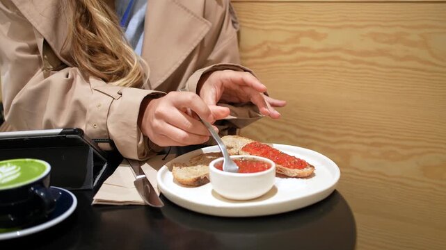 Businesswoman eating pan con tomate, traditional spanish toast with tomato, while having breakfast in a cafe with a matcha green tea latte and using a tablet for work