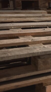 Rough Timber Storage. Wooden Pallets In Industrial Setting. Dim Warehouse With Stacked Wooden Shipping Pallets. Media
