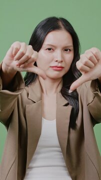 A business woman gives a double thumbs-down with a disappointed expression on a green screen. Great for failure, rejection, and negative feedback concepts.