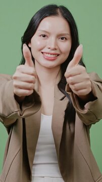 A cheerful business woman gives a double thumbs-up against a green background. Ideal for business success, positive review, and approval content.