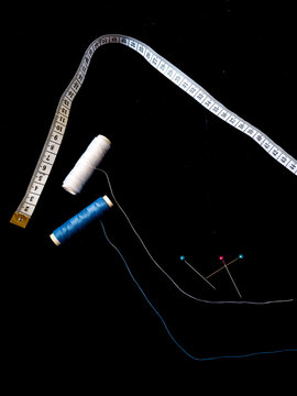 Wei&szlig;er und blauer Faden, Ma&szlig;band und Stecknadeln auf schwarzen Stoff Hintergrund