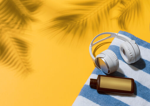 Headphones and Sunscreen on Beach Towel with Tropical Palm Shadow