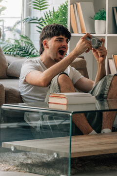 Young person or student sitting in the living room of home playing excitedly online with mobile phone or smartphone