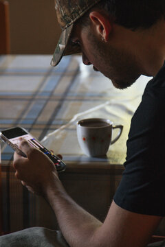 Young person indoors typing on a smartphone with a cup of coffee