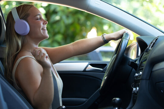 woman driving a car while wearing wireless headphones, smiling and enjoying music during a road trip