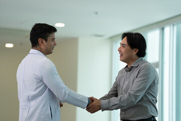 Doctor greeting male patient with handshake during medical consultation in hospital corridor in bright clinical setting © Stock Media Labs