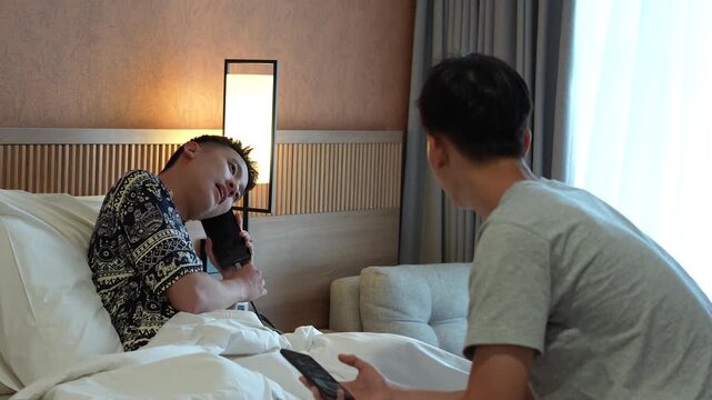 shot of two young Asian men in a hotel room looking panic or urgent with one making a phone call on his charging smartphone and with his brothers holding phone 