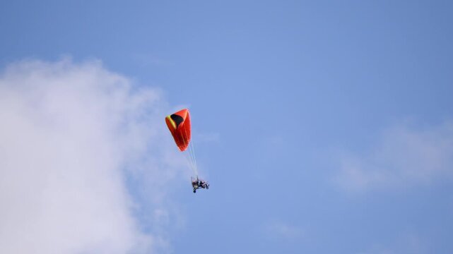 Paraglider soars above clouds with vivid red canopy. Sky dancer glides calmly through crisp blue air. Freedom and adventure echo in every soaring movement. Ideal for thrill-seeking, outdoor adventure