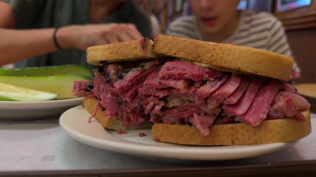 Delicious pastrami on rye sandwich served on a plate at a classic new york deli, with a child in the background eagerly waiting to eat the famous traditional meal