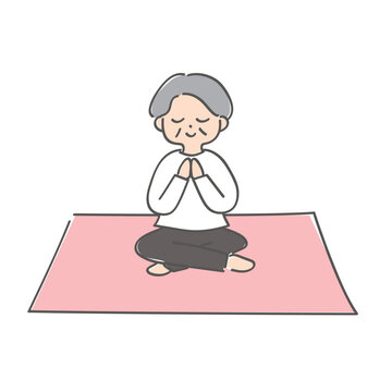 ヨガマットの上で合掌のポーズをしているおばあさん