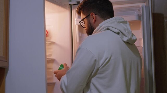 Man checks and organizes food inside an open refrigerator, showing household food storage, kitchen routine, grocery management and daily life at home.