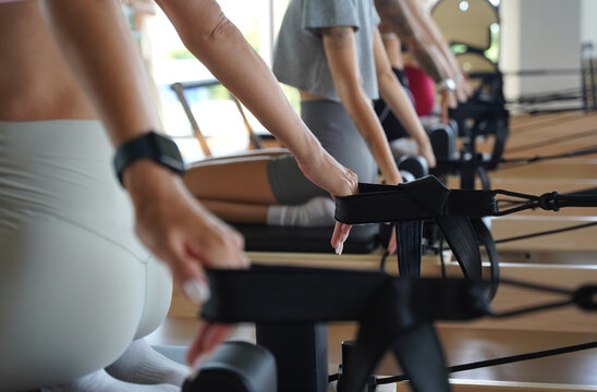 A group of young women perform pilates exercises on reformer machines under the guidance of a coach