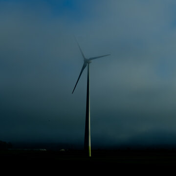 Single wind turbine rising above fields in blue winter haze