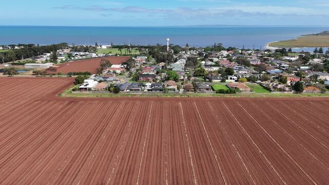 Aerial drone view over freshly ploughed farmland with long parallel furrows at Werribee South, Melbourne,  Australia, with the suburban homes behind the field. Agricultural land meeting coastal suburb