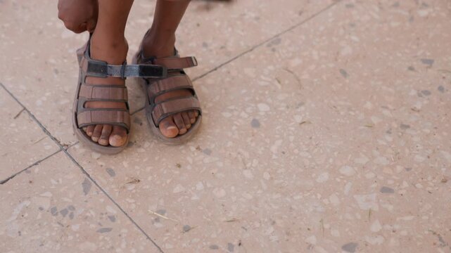 Close up shows person hands and lower legs as they adjust sandal straps. scene focuses solely on this repetitive detailed interaction with footwear against plain tiled floor