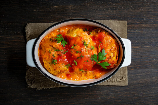 Homemade meatballs in tomato sauce served in ceramic dish top view. Baked meatballs or cutlets with red gravy and fresh herbs. Delicious traditional hot meal in white plate on wooden background