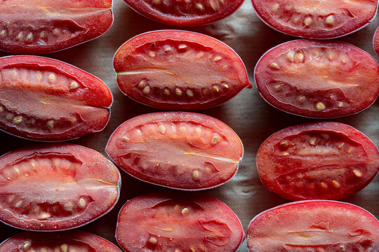 Frozen sliced red tomatoes with hoarfrost texture, closeup. Cut tomato halves covered with ice crystals. Organic frozen vegetables backdrop for food storage, preservation and healthy eating concepts