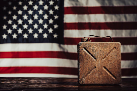 Vintage rusty fuel canister with American flag. Old rusty jerrycan on wooden table. Defocused USA flag background for american oil industry, fuel crisis, energy policy or vintage history concept