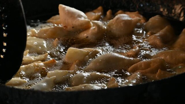 Samosas deep frying in a large iron wok. Golden, crispy samosas deep-frying to perfection in hot bubbling oil inside a traditional iron wok. It is a fried pastry filled with a spiced and potato.