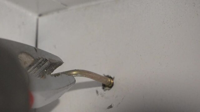 Metal pliers removing a bent wall anchor from a white interior surface during home renovation. Extreme macro tight handheld close-up shot.