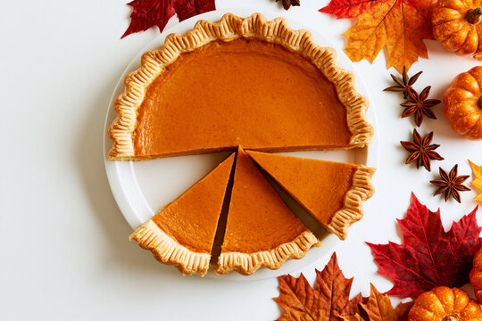 Sliced pumpkin pie with autumn leaves, star anise and mini pumpkins, Thanksgiving flat lay
