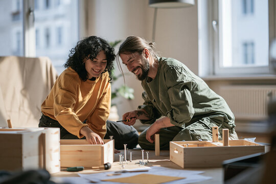 Young couple assembling flat pack furniture together on the floor of a bright apartment living room