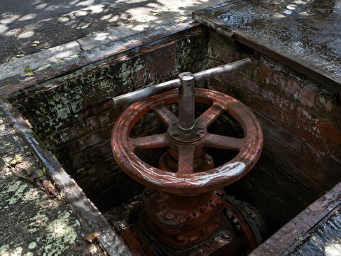 Large municipal water main valve wheel with a valve key wrench on the spindle and a chalk mark across the rim
