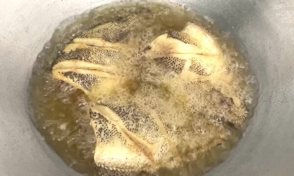 Close up of crispy whole gourami fish (pla salid) deep fried in hot boiling oil in a pan, traditional Thai home cooking and delicious local food.