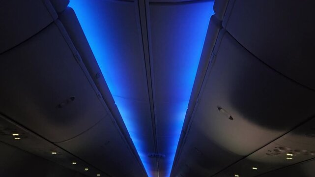 Blue ambient LED lighting illuminates the aircraft cabin ceiling and overhead bins, conveying a calm, modern atmosphere during a night flight. Ideal for travel, aviation, and transportation concepts.