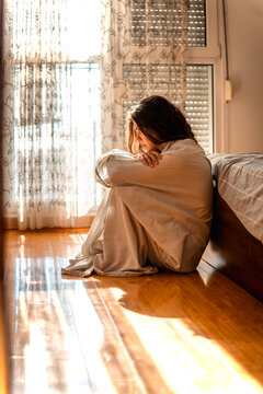 Sad lonely female feeling down, sitting on bedroom floor wrapped in bedsheet. Apathy, grief and despair.