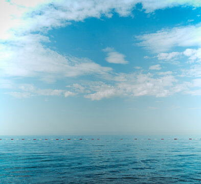 Minimalist seascape with red buoys floating on calm sea water under a cloudy sky.