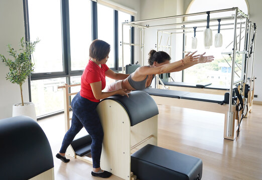 A young woman perform pilates exercises on spine corrector under the guidance of a coach