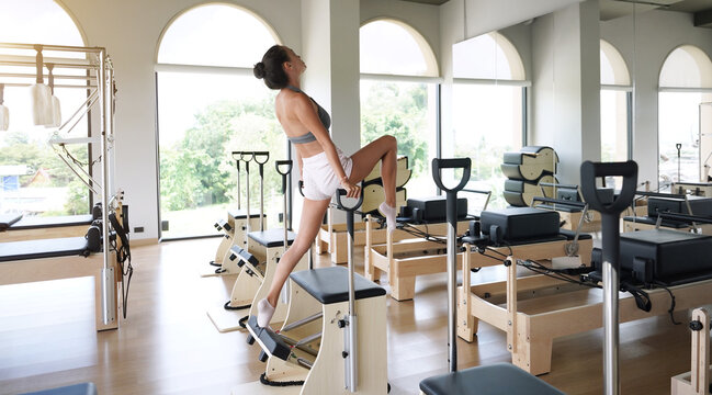 A young woman perform pilates exercises on wunda chair in a gym with large windows