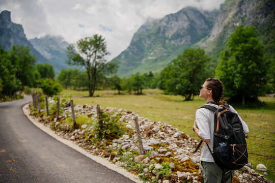 Young caucasian woman hiker with backpack walking on a trail with a beautiful mountain view.