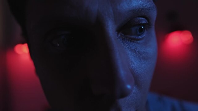 Anxious man with restless eyes constantly looking around and turning toward a possible threat, portraying hypervigilance, fear, paranoia and anticipation in a blue and red low key close up