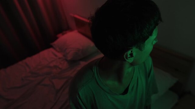 Anxious man nervously looking around his bedroom, scanning the room for danger while expecting a threatening event, expressing hypervigilance, fear and paranoia in red and green low key light