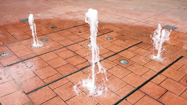 Slow motion water fountain erupting from red paved ground