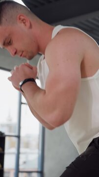 Man in gym setting focusing on upper body. subject is wearing white tank top and black wristband with clenched fist suggesting preparation for workout or strength training