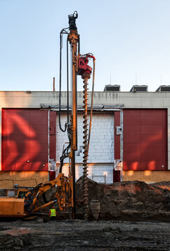 Foundation drilling and ground engineering beside a building at an urban construction site. A rotary drilling rig with a large auger prepares the ground for foundation and work during redevelopment